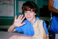 Adam waving to the camera at what appears to be a school desk. Based on the T-Shirt, this image was taken in 2005, during the short period Adam spent at St.Rose of Lima School.